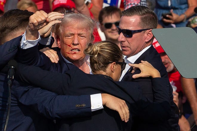 US Republican candidate Donald Trump is seen with blood on his face, surrounded by secret service agents as he is taken off the stage at a campaign event at Butler Farm Show Inc. in Butler, Pennsylvania, on July 13, 2024. Trump was hit in the ear in an apparent assassination attempt by a gunman at a campaign rally on Saturday, in a chaotic and shocking incident that will fuel fears of instability ahead of the 2024 US presidential election. The 78-year-old former president was rushed off stage with blood smeared across his face after the shooting in Butler, Pennsylvania, while the gunman and a bystander were killed and two spectators critically injured.