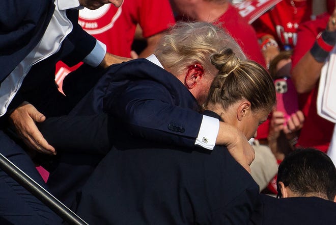 US Republican candidate Donald Trump is seen with blood on his face, surrounded by secret service agents as he is taken off the stage at a campaign event at Butler Farm Show Inc. in Butler, Pennsylvania, on July 13, 2024. Trump was hit in the ear in an apparent assassination attempt by a gunman at a campaign rally on Saturday, in a chaotic and shocking incident that will fuel fears of instability ahead of the 2024 US presidential election. The 78-year-old former president was rushed off stage with blood smeared across his face after the shooting in Butler, Pennsylvania, while the gunman and a bystander were killed and two spectators critically injured.