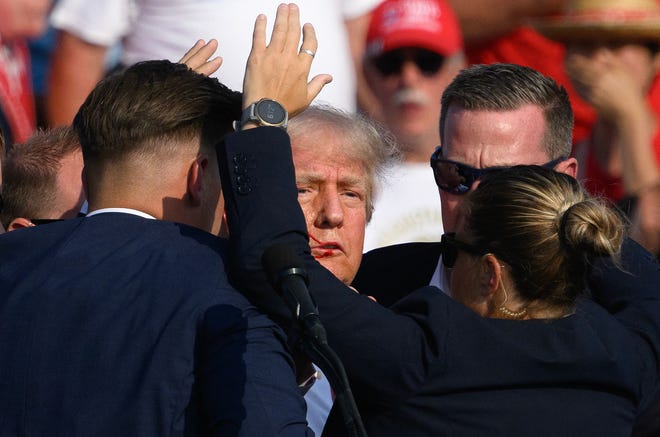 Secret Service agents surround Republican presidential candidate former President Donald Trump onstage after he was grazed by a bullet at a rally on July 13, 2024, in Butler, Pennsylvania. Butler County District Attorney Richard Goldinger said the shooter is dead after grazing former President Trump with a bullet, killing one audience member and injuring another in the shooting.