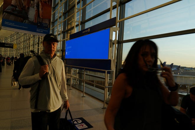 Travelers walk past a departures board displaying a blue error screen inside Terminal C in Newark International Airport, after United Airlines and other airlines grounded flights due to a worldwide tech outage caused by an update to Crowdstrike's "Falcon Sensor" software which crashed Microsoft Windows systems, in Newark, New Jersey, U.S., July 19, 2024. REUTERS/Bing Guan