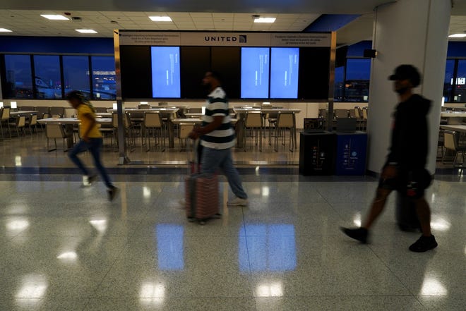 Travelers walk past a departures board displaying blue error screens, also known as the "Blue Screen of Death" inside Terminal C in Newark International Airport, after United Airlines and other airlines grounded flights due to a worldwide tech outage caused by an update to Crowdstrike's "Falcon Sensor" software which crashed Microsoft Windows systems, in Newark, New Jersey, U.S., July 19, 2024.