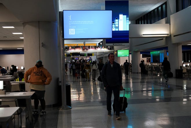 Travelers walk past a monitor displaying a blue error screen inside Terminal C in Newark International Airport, after United Airlines and other airlines grounded flights due to a worldwide tech outage caused by an update to Crowdstrike's "Falcon Sensor" software which crashed Microsoft Windows systems, in Newark, New Jersey, U.S., July 19, 2024.