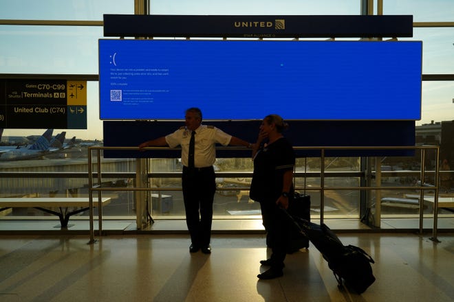 United Airlines employees wait by a departures monitor displaying a blue error screen inside Terminal C in Newark International Airport, after United Airlines and other airlines grounded flights due to a worldwide tech outage caused by an update to Crowdstrike's "Falcon Sensor" software which crashed Microsoft Windows systems, in Newark, New Jersey, U.S., July 19, 2024.