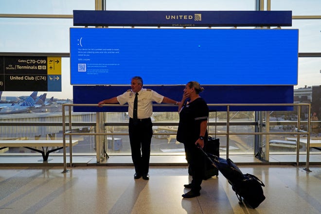 United Airlines employees wait by a departures monitor displaying a blue error screen, also known as the “blue screen of death,” inside Terminal C in Newark International Airport, after United Airlines and other airlines grounded flights due to a worldwide tech outage caused by an update to CrowdStrike's "Falcon Sensor" software which crashed Microsoft Windows systems, in Newark, New Jersey, on July 19, 2024.